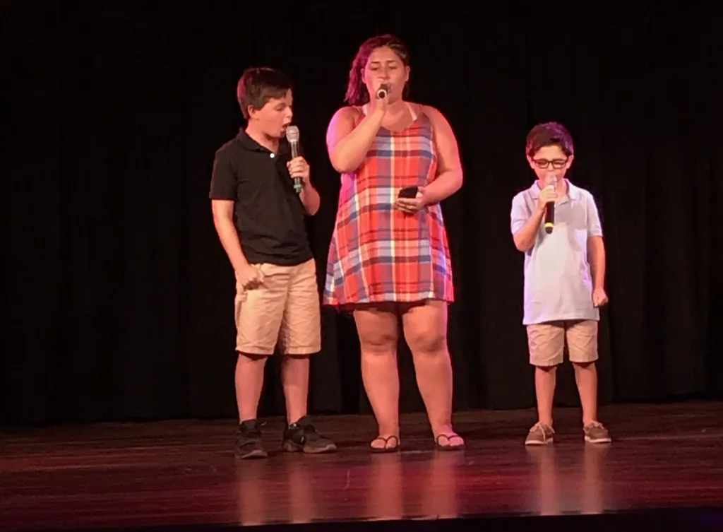 Three young people singing on a stage with microphones.