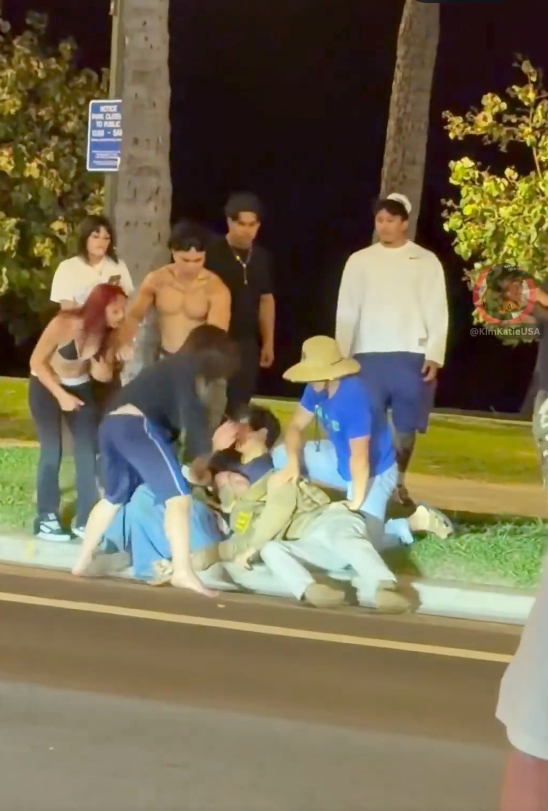 A group of people assaulting a man in an ICE uniform on the ground at night in Honolulu.