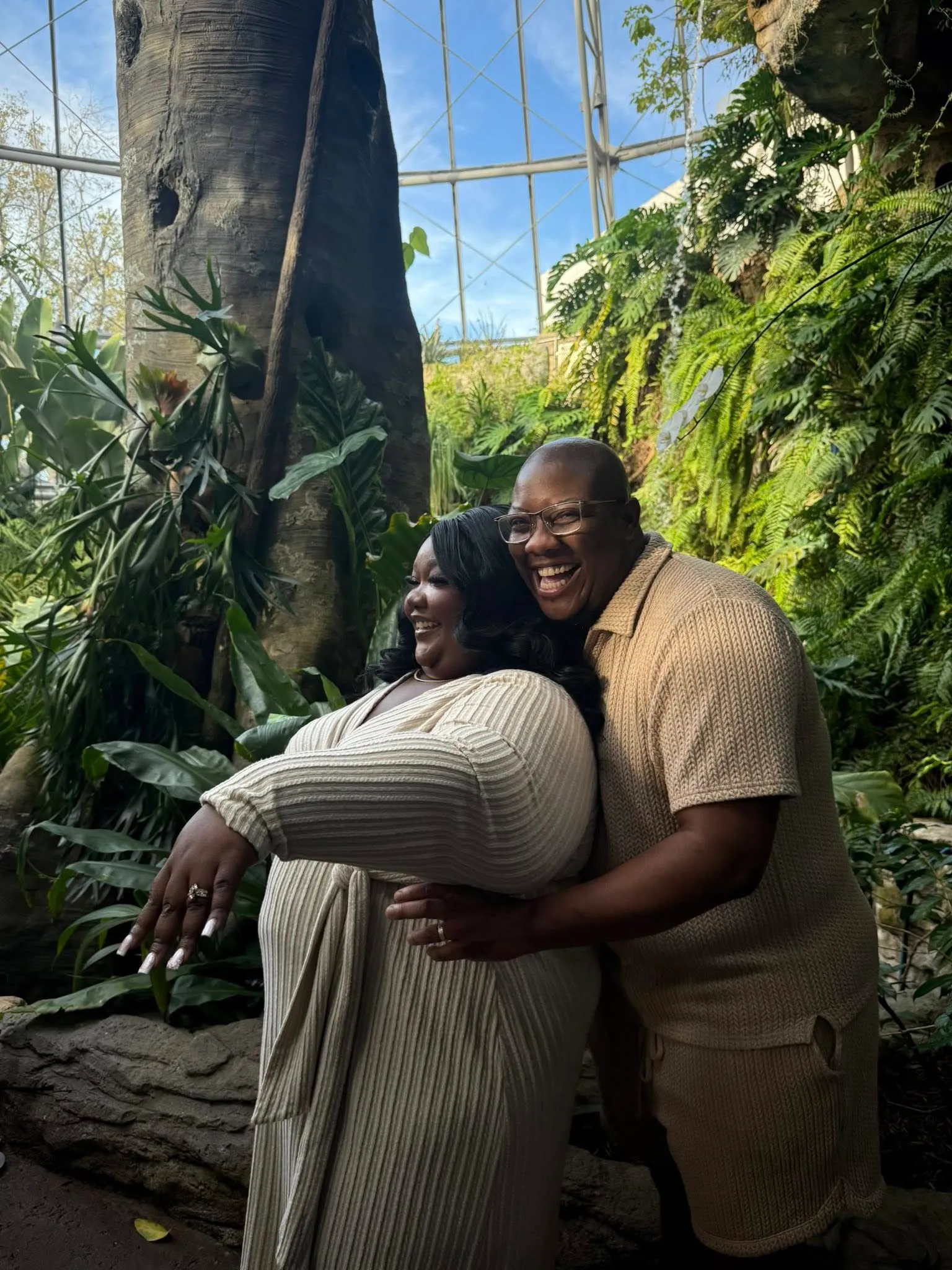 A man and a woman pose in front of greenery after an engagement