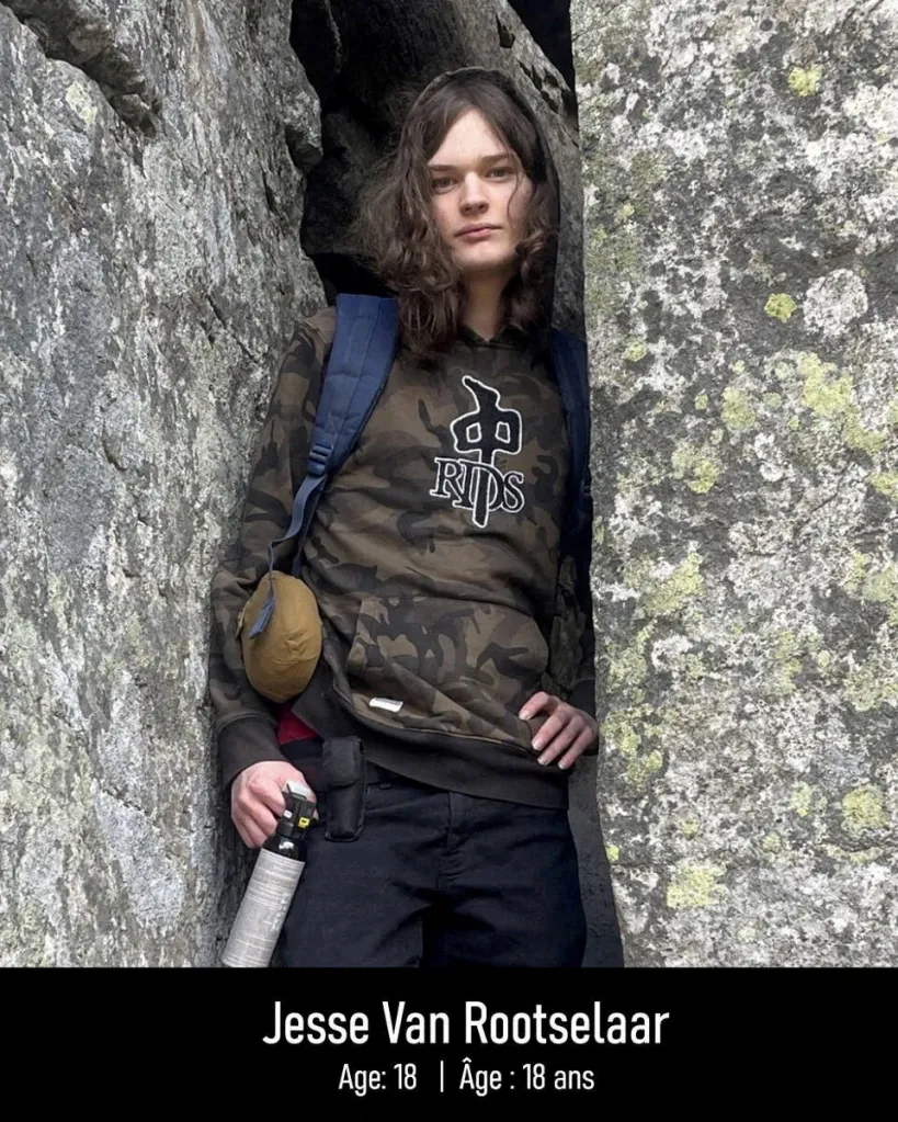 Jesse Van Rootselaar, 18, wearing a camouflage hoodie and holding a canister, standing between two large rocks.