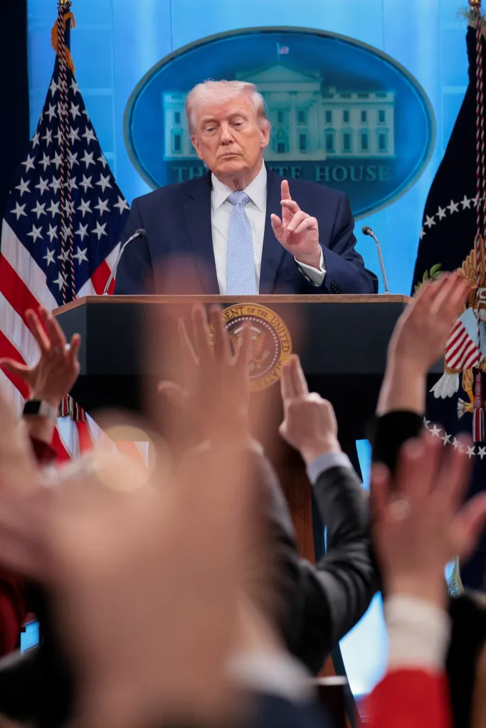 President Trump holds a press conference at the White House with hands raised in the foreground.