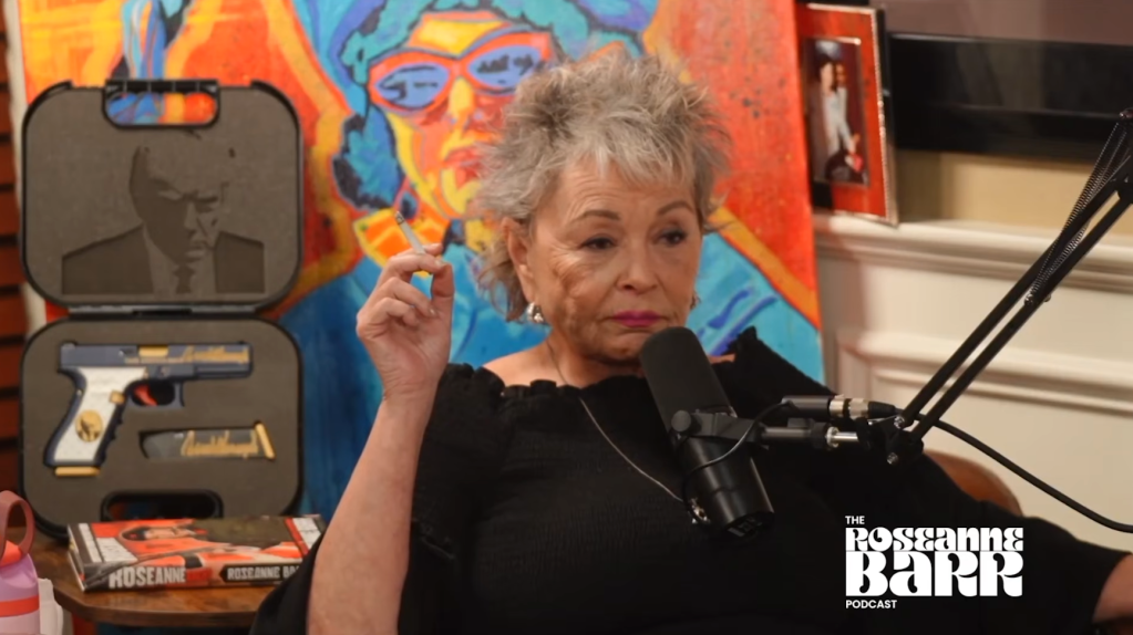 Roseanne Barr smoking with a gun in a case featuring Donald Trump and a portrait behind her.