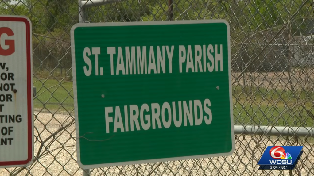 A green sign on a chain-link fence reads 