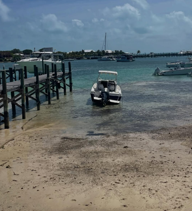 A motorboat tied to a wooden dock with several other boats and buildings visible in the background under a cloudy sky.