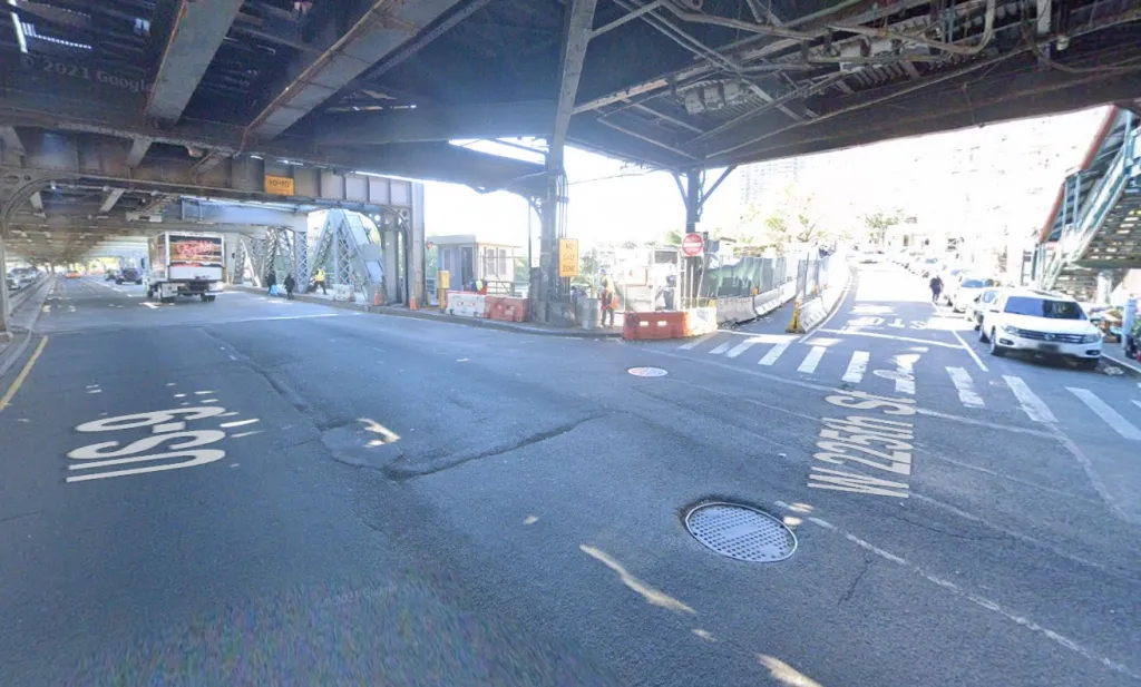 A street view of a road intersecting with West 225th Street in New York, passing under an elevated train track.