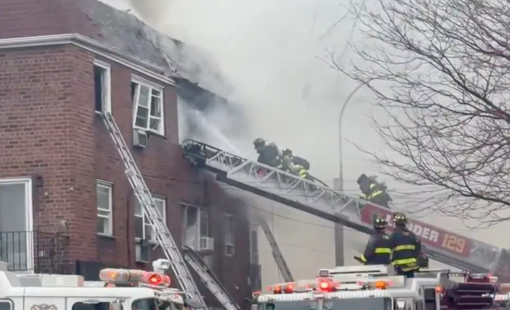 Firefighters battling a large fire in an apartment building, with ladders extended and smoke billowing from the roof.
