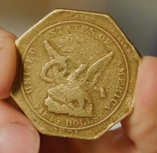 A person holding an octagonal gold coin from 1851 with the words 