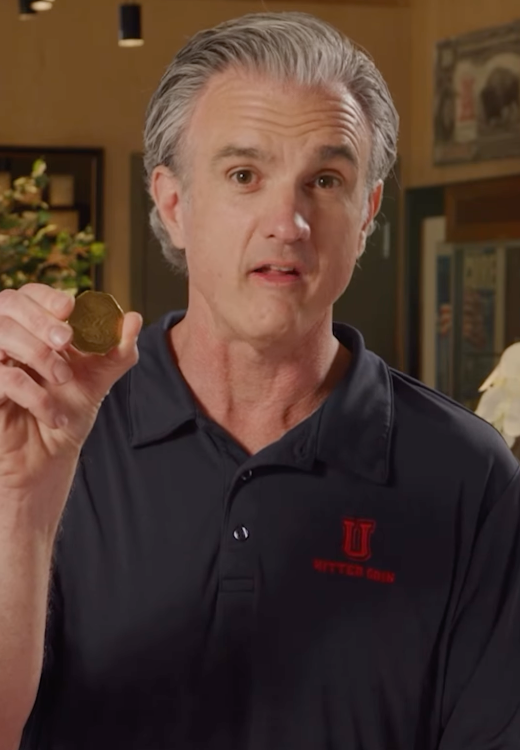 A man with grey hair holding a gold coin.