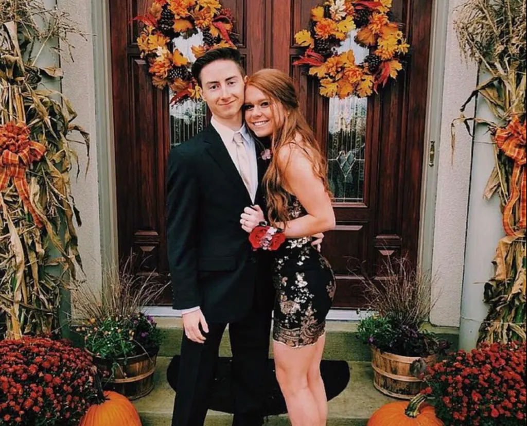 A young man in a suit and a young woman in a sparkly dress posing in front of a decorated door.