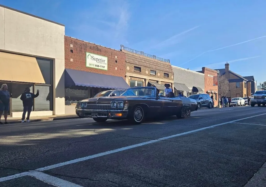 A brown convertible car driving past a building with a 