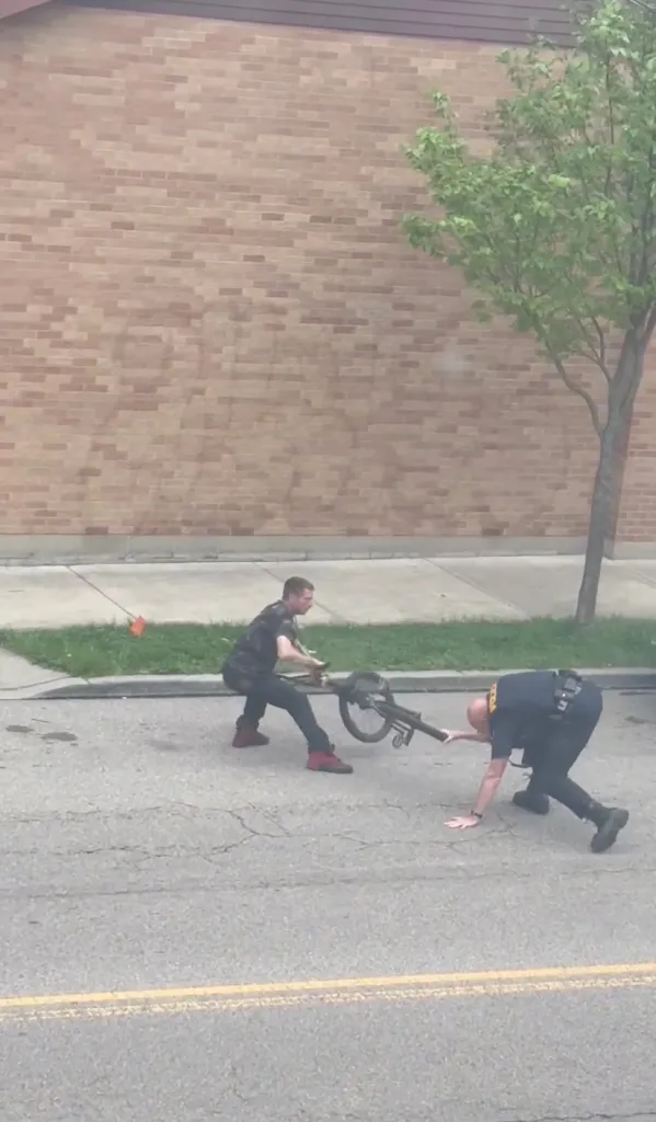 A man swinging a bicycle at a police officer who is on his hands and knees.