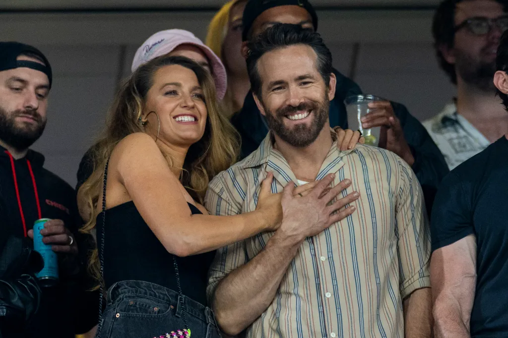 Blake Lively and Ryan Reynolds smiling and embracing at a stadium.