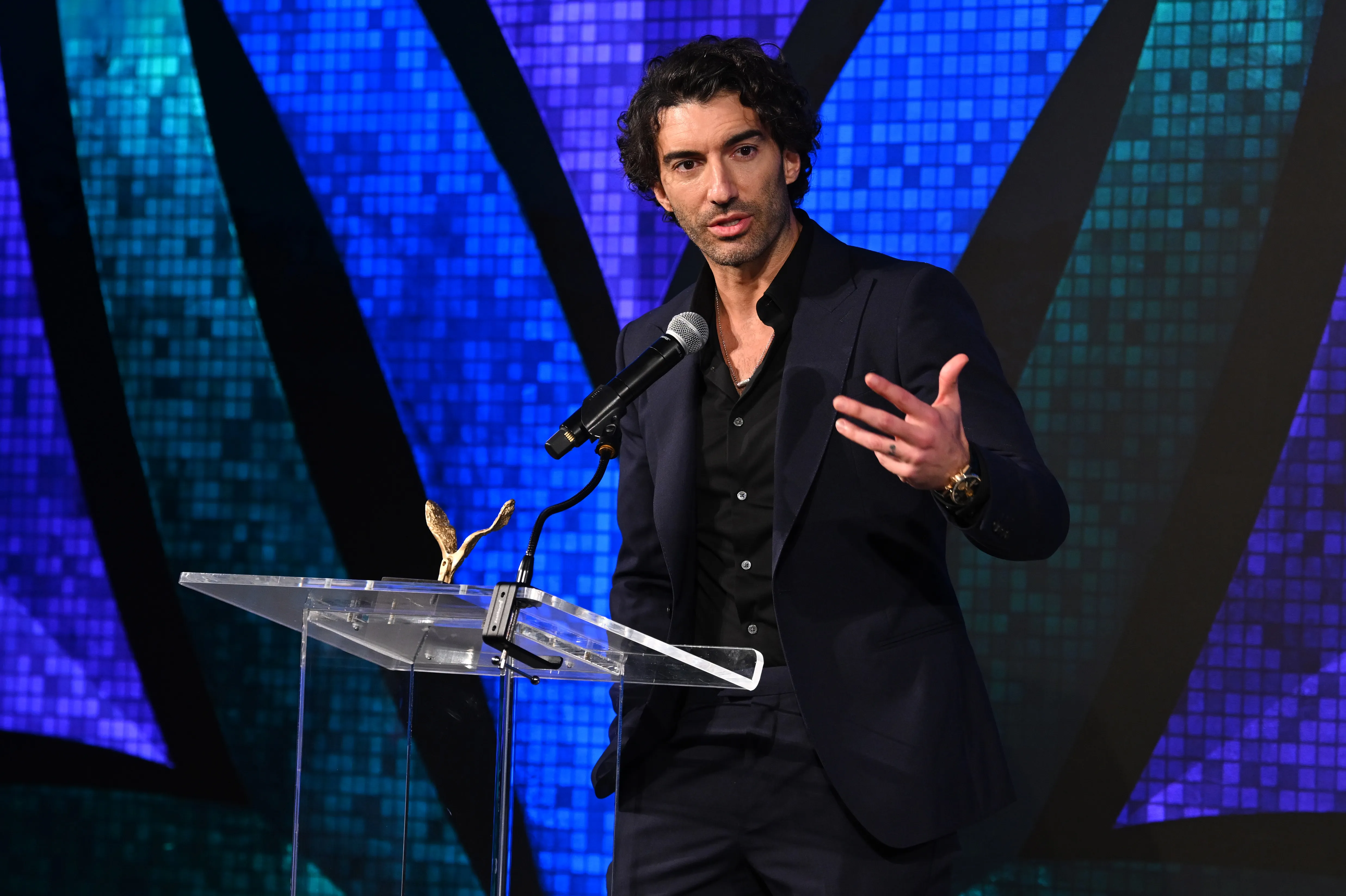 Actor Justin Baldoni speaking at a podium.