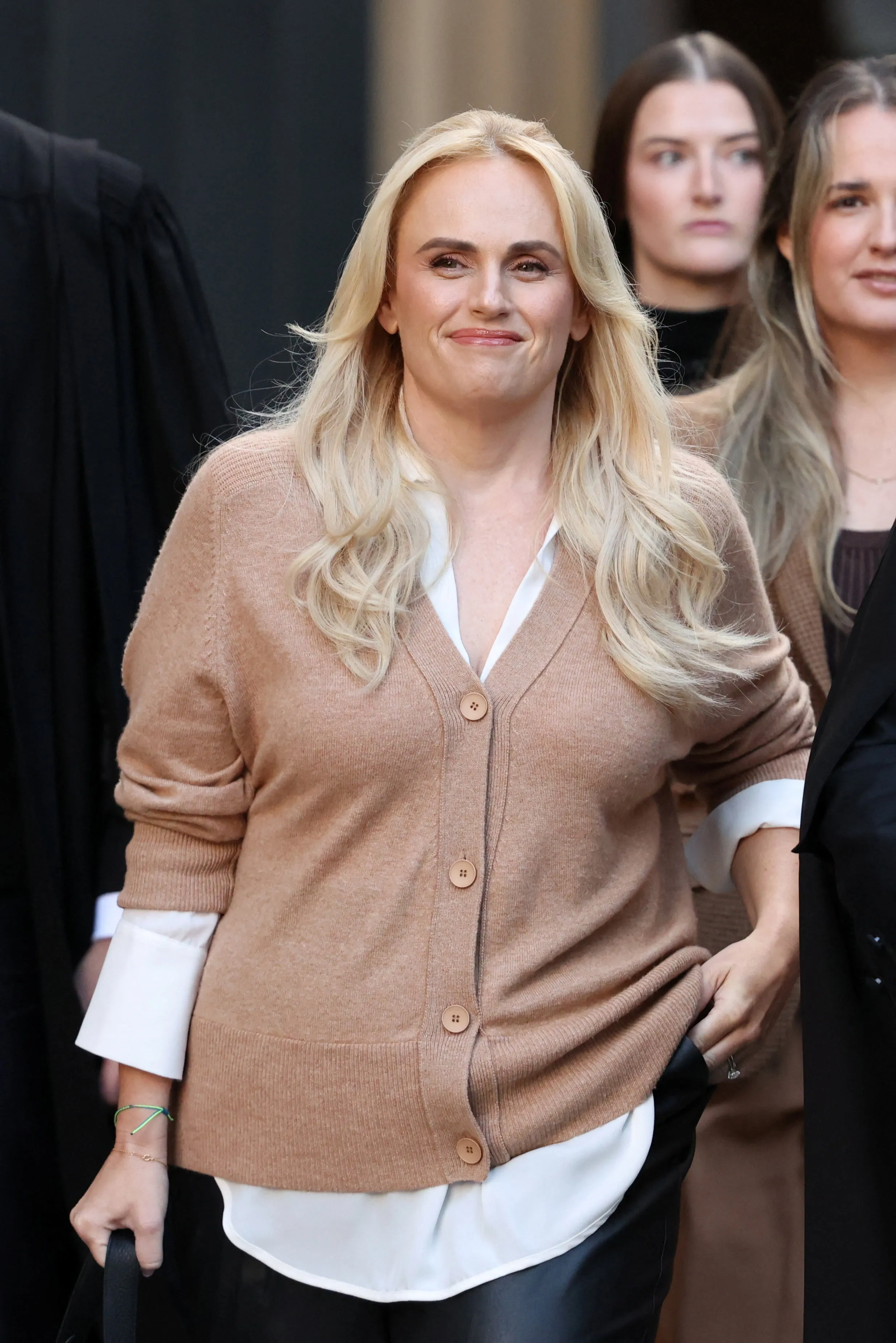 Rebel Wilson arrives at court for a defamation hearing, wearing a brown cardigan over a white shirt.