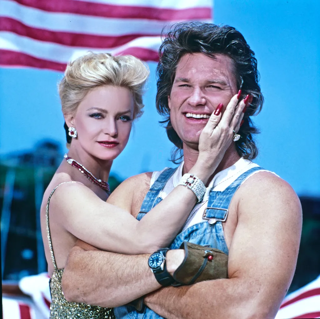 Goldie Hawn and Kurt Russell posing for a portrait against an American flag.