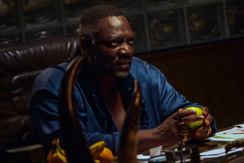 Adewale Akinnuoye-Agbaje in a blue robe, holding an apple.