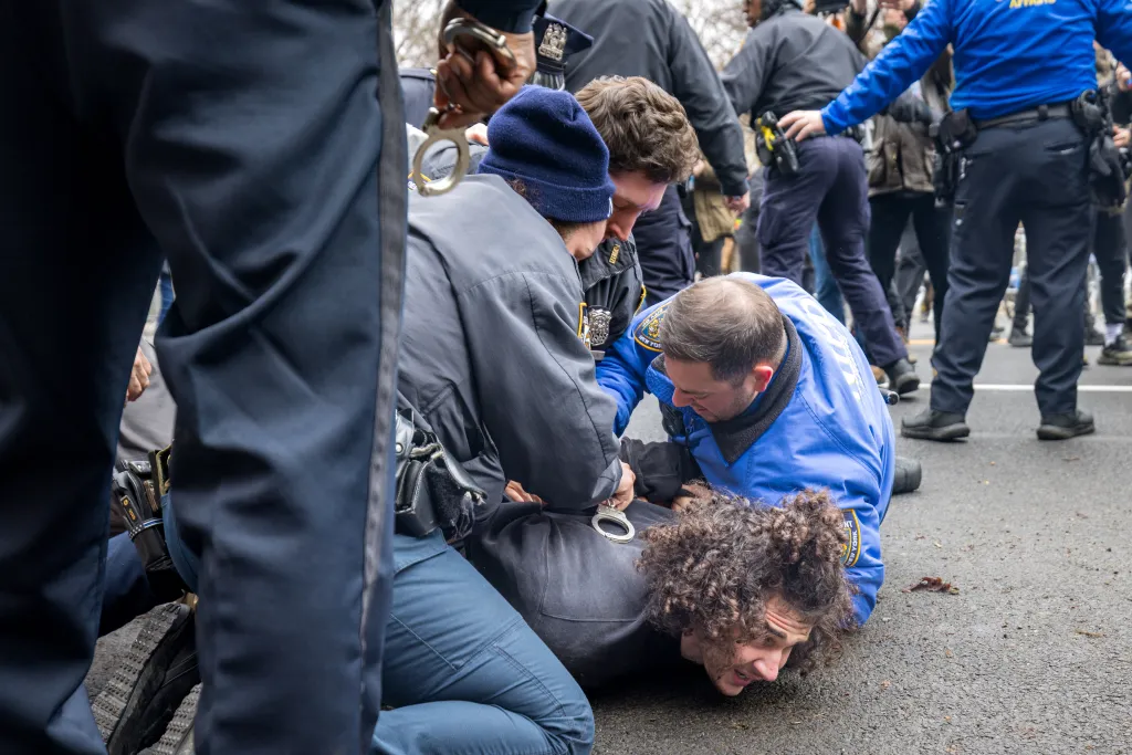 Police officers arresting a man with curly hair and a dark shirt on the ground.