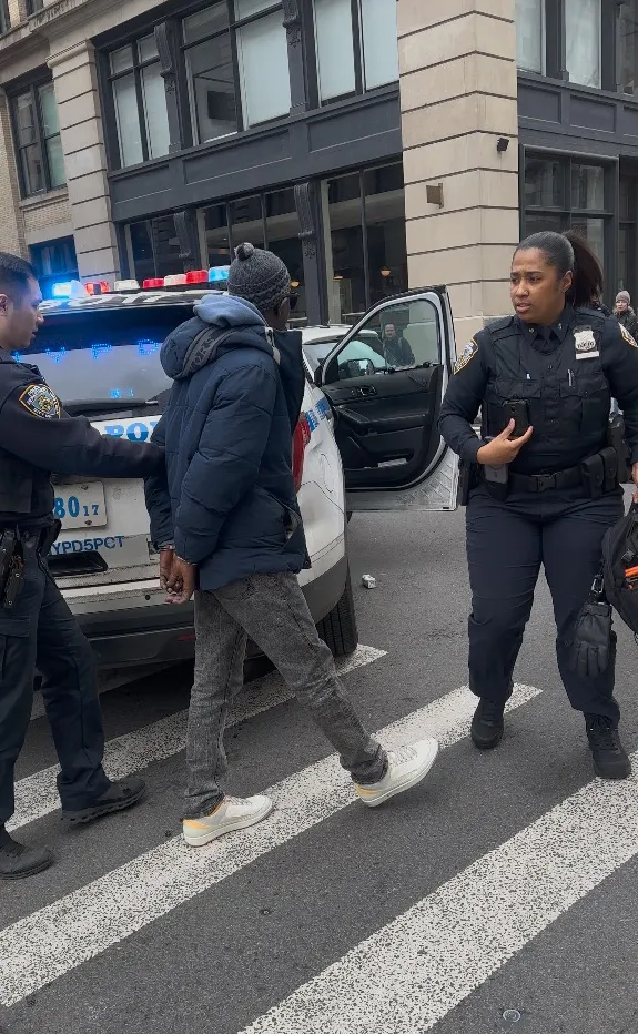 A man in handcuffs being led by police officers on a city street.