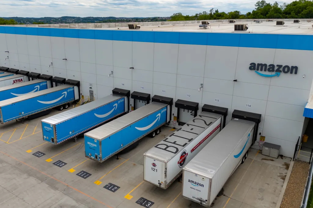 Aerial view of an Amazon distribution center with multiple Prime delivery trucks backed into loading docks.
