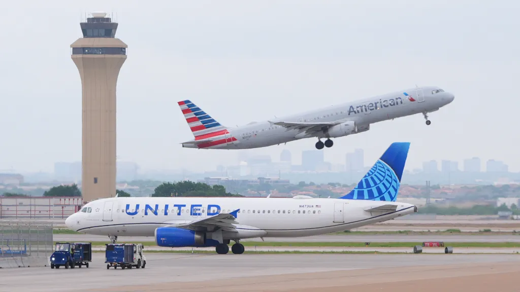 An American Airlines jet takes off while a United Airlines jet taxis at DFW International Airport.