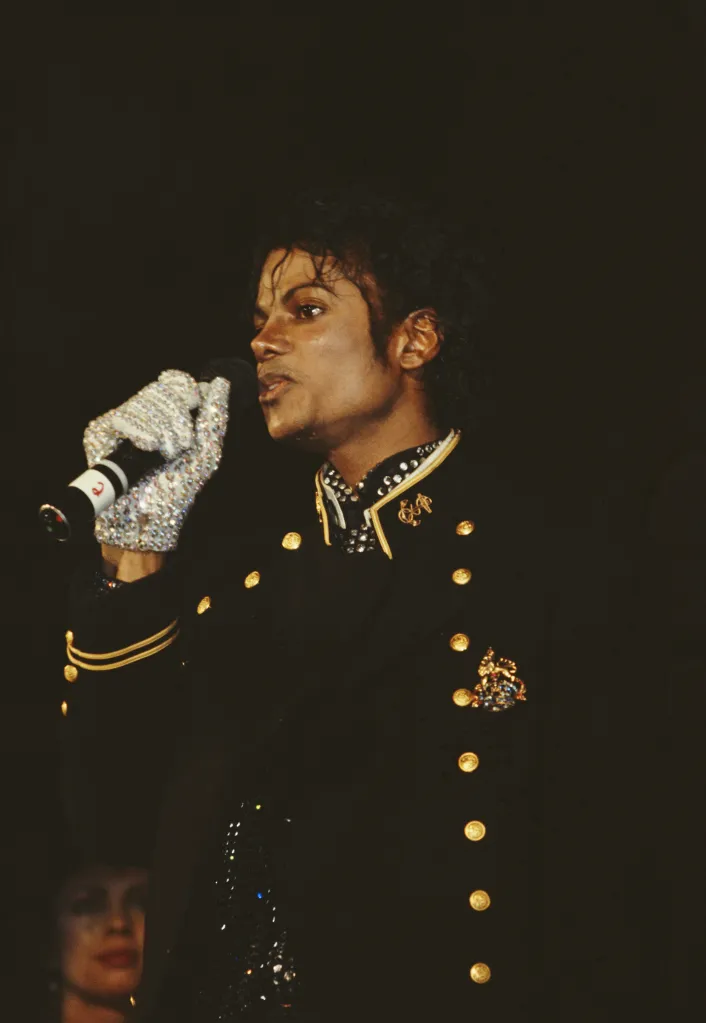 Michael Jackson singing into a microphone, wearing a sequined glove and military-style jacket.