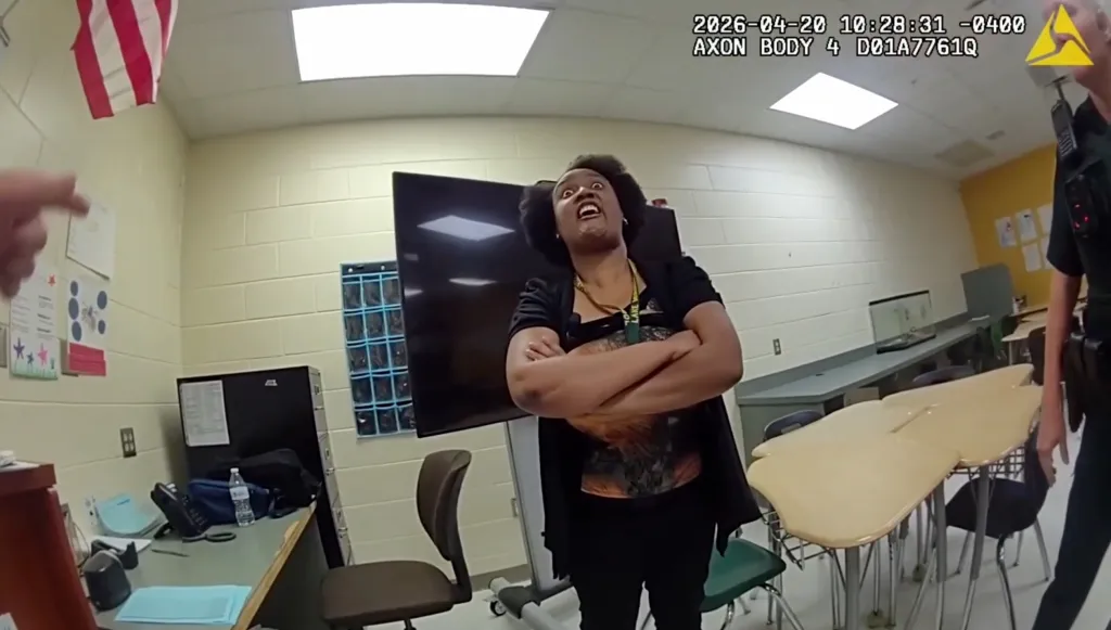 Bodycam footage shows Angela Jourdan looking up with her mouth open and arms crossed in a classroom with a police officer.