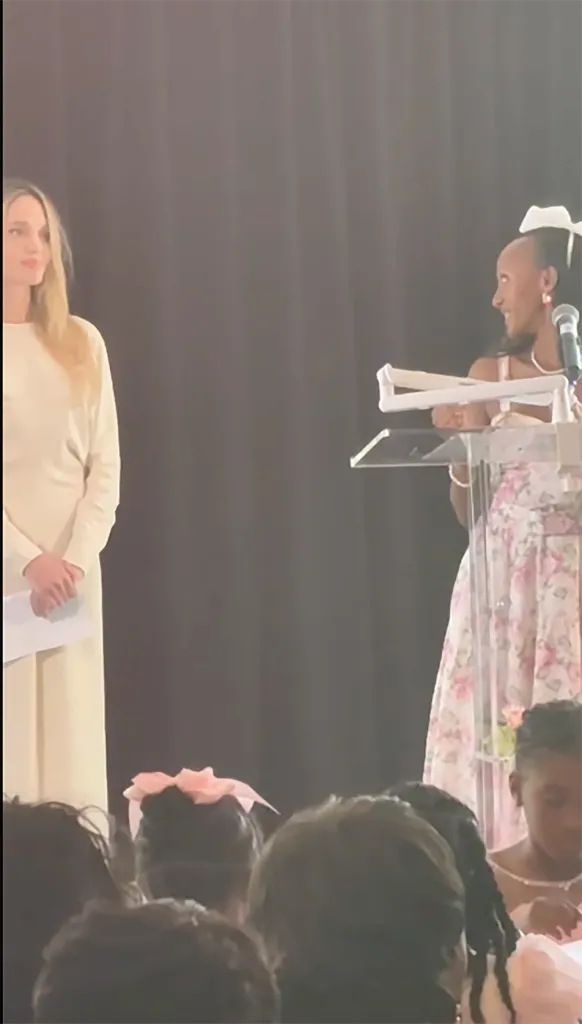 Zahara Jolie-Pitt giving a speech at a podium as Angelina Jolie stands nearby.