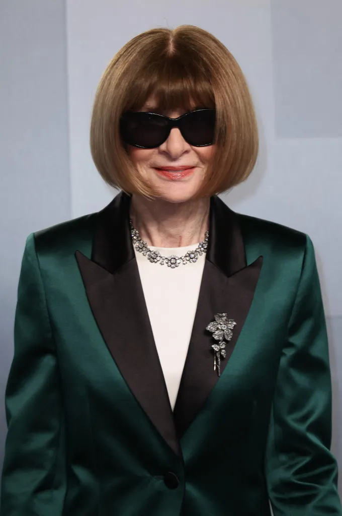 Anna Wintour in a dark green and black suit and sunglasses.