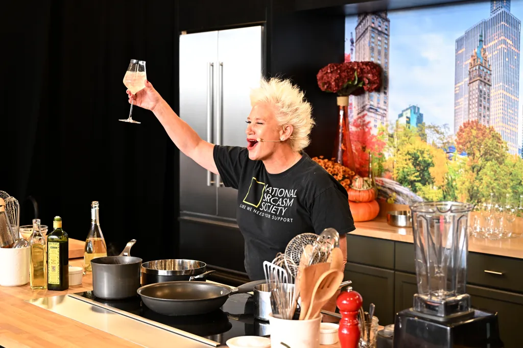 Chef Anne Burrell making a culinary presentation while holding a wine glass.
