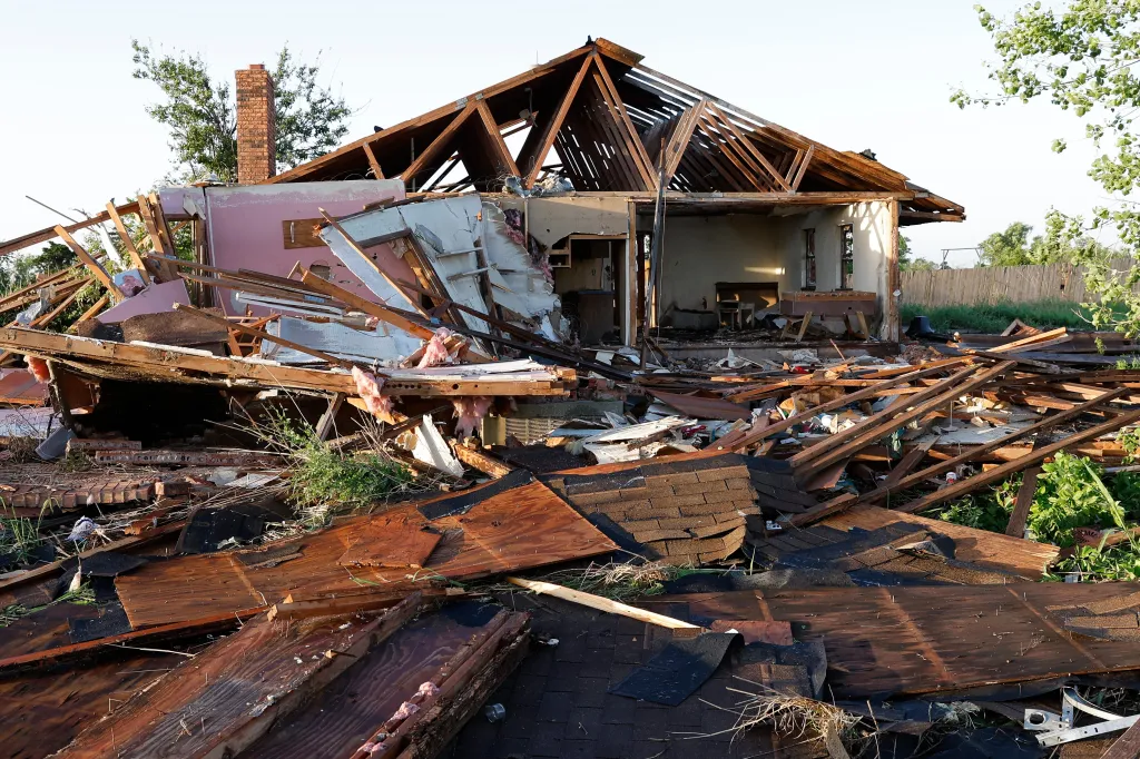 A home in Enid, Oklahoma, heavily damaged by a tornado, with the roof destroyed and debris scattered around.