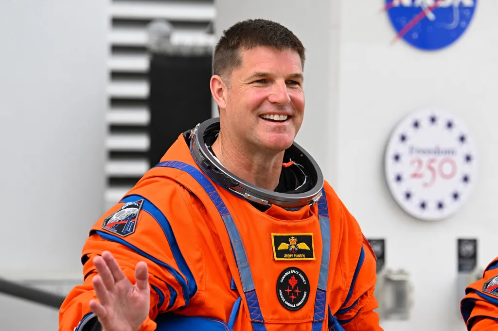 A smiling male astronaut with dark hair in an orange space suit
