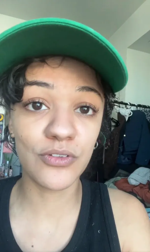 Marissa Bode, a woman with curly hair and a green cap, talks directly to the camera.