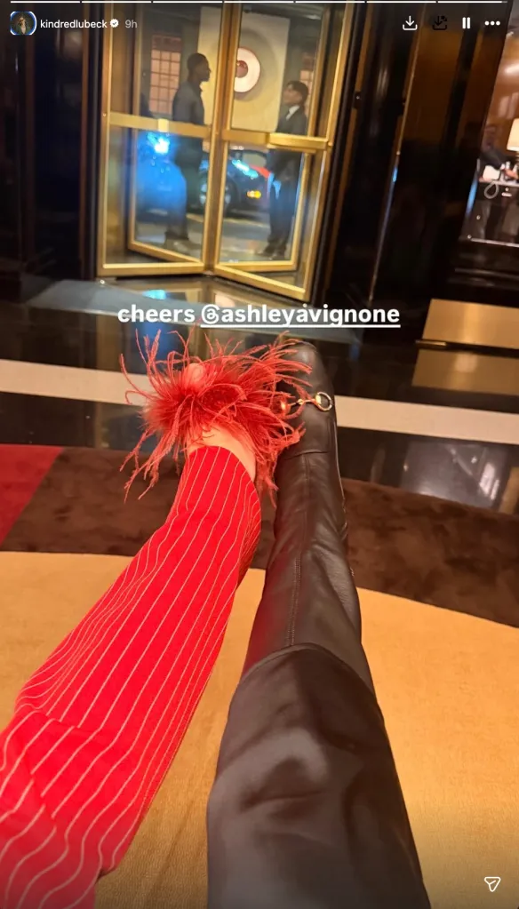 A person in a red and white striped top with a red feathered cuff and a person in a black boot with a gold buckle are shown with their legs crossed, the background shows the reflection of two men in a revolving glass door.