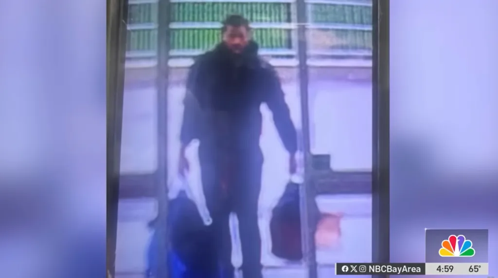 Security camera footage of a man in dark clothing carrying bags.