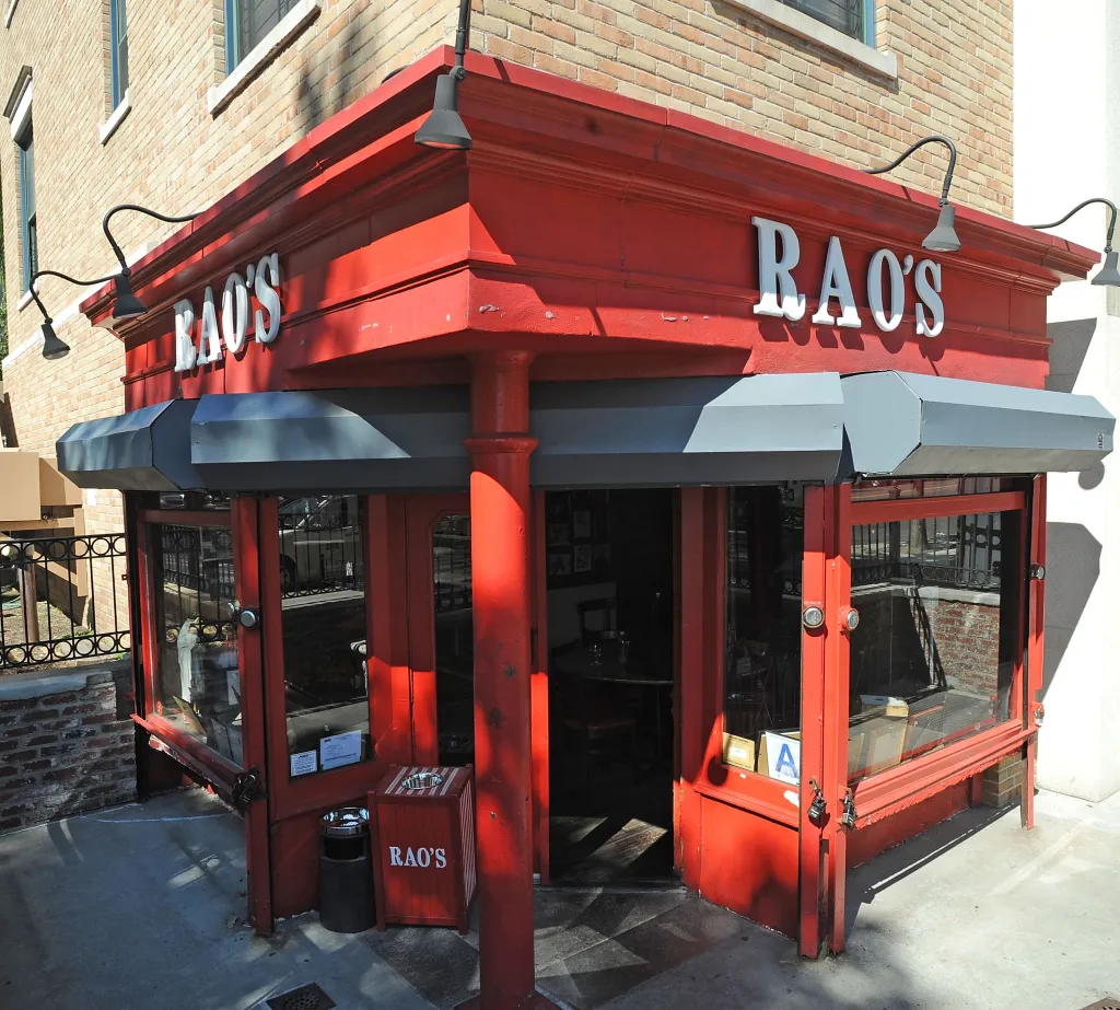 Exterior of Rao's restaurant with a red facade and white awning, in New York City.