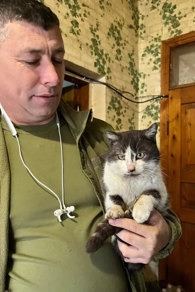 A man in a green shirt holding a black and white cat