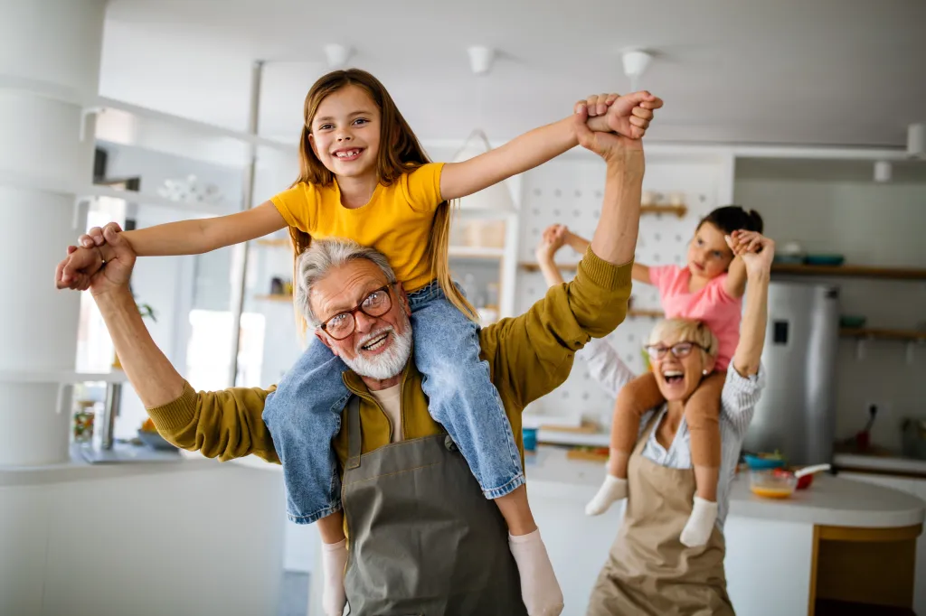 Grandparents happily playing with their grandchildren, carrying them on their shoulders.