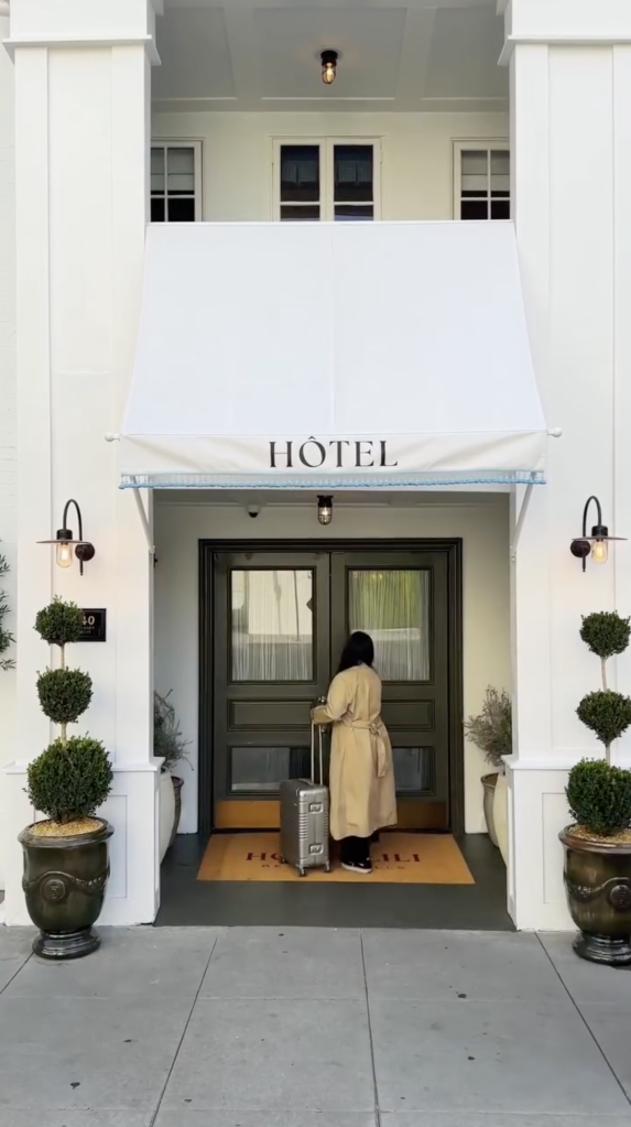 A person with a suitcase approaches the entrance of a building with an awning that says
