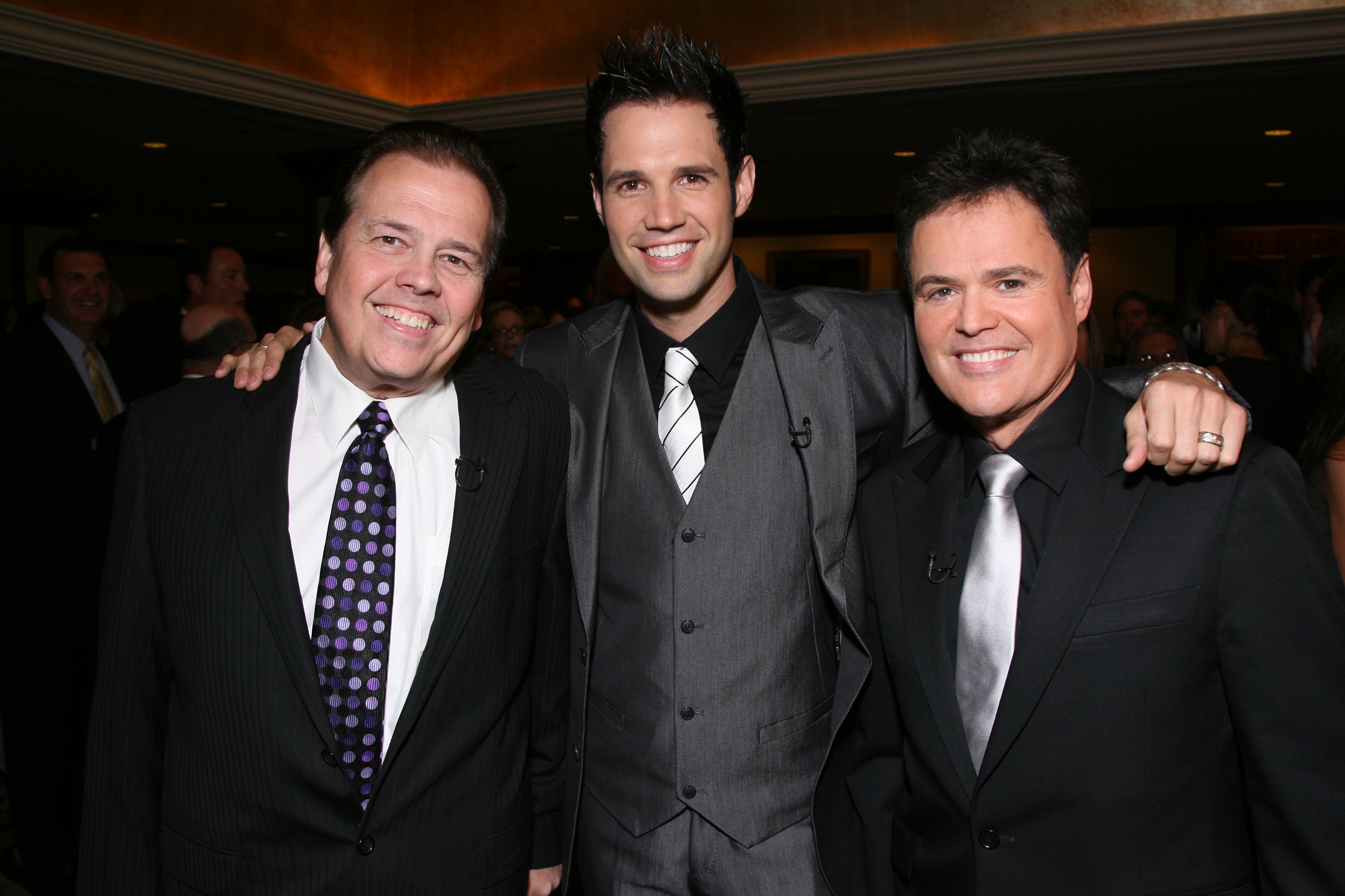 Alan Osmond and his son sit on a couch smiling.