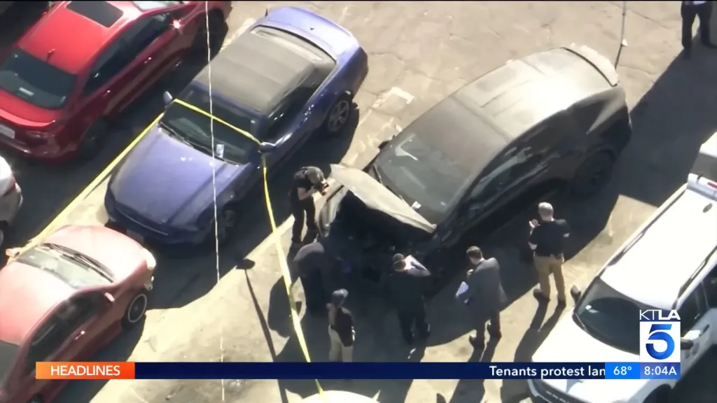 Overhead view of police investigating a black Tesla with its hood open, surrounded by yellow police tape.