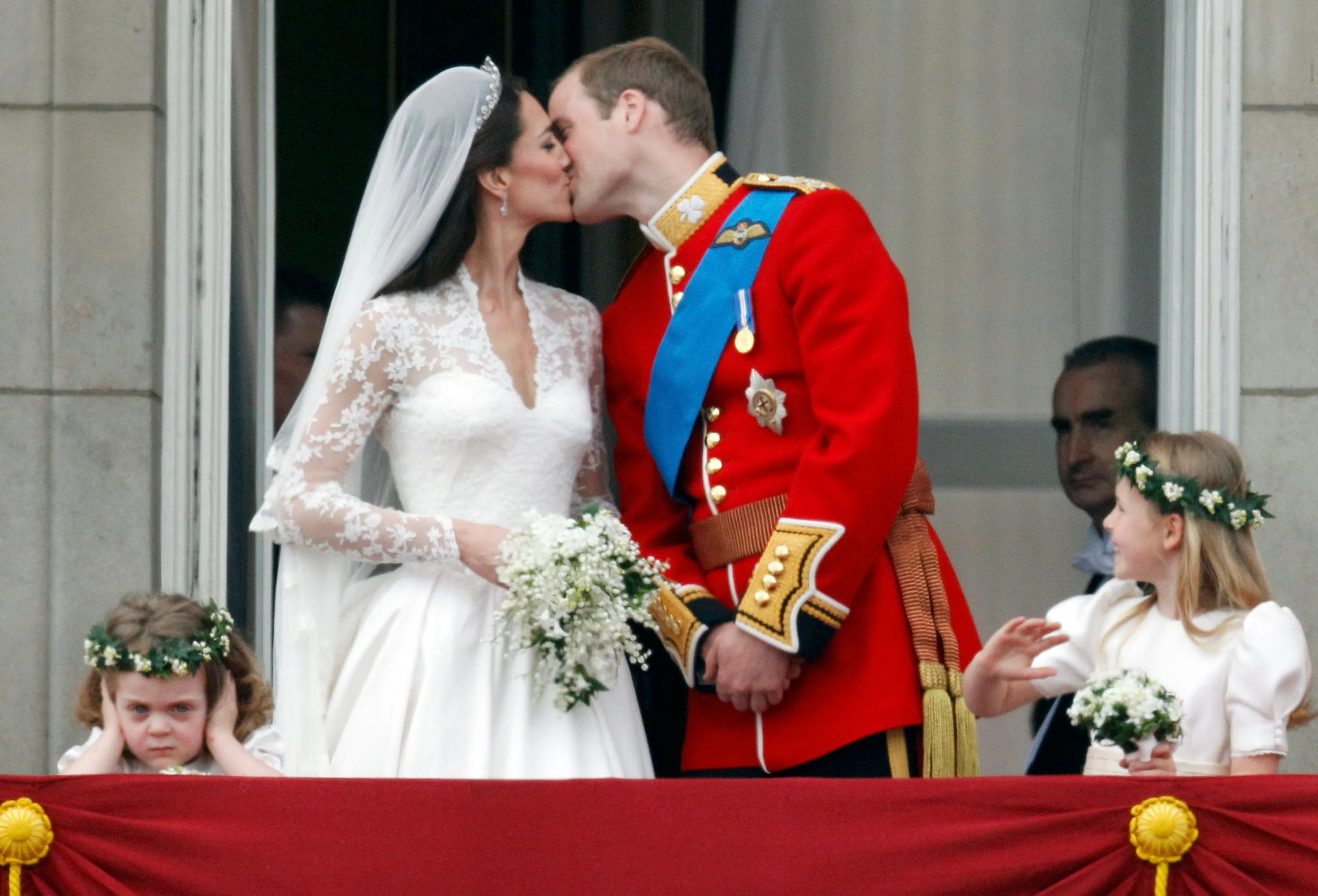 Prince William and Catherine kiss on the balcony of Buckingham Palace, with two young bridesmaids beside them.