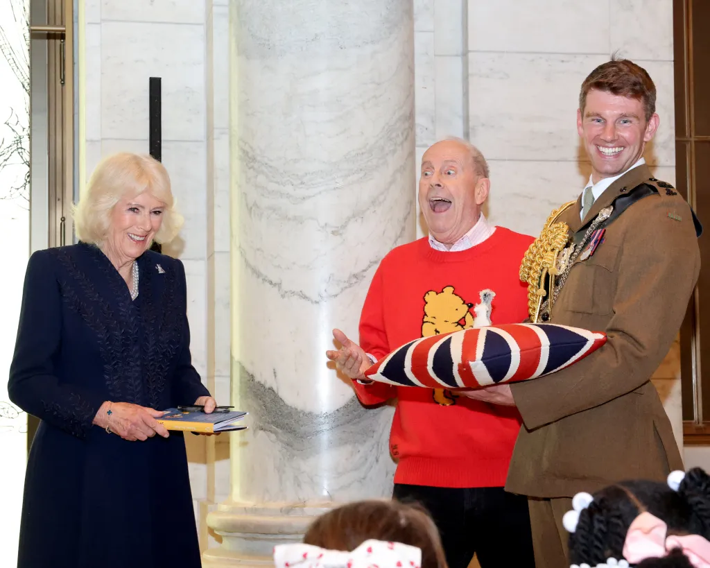 Queen Camilla, in a navy dress, holds a copy of 