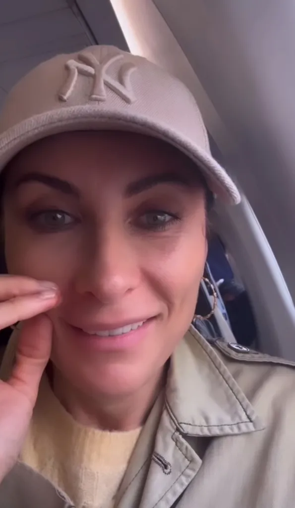 Laura Benanti in a baseball cap and trench coat on a plane.