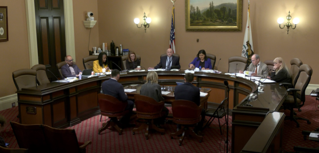 People seated around a large U-shaped table at a budget hearing.