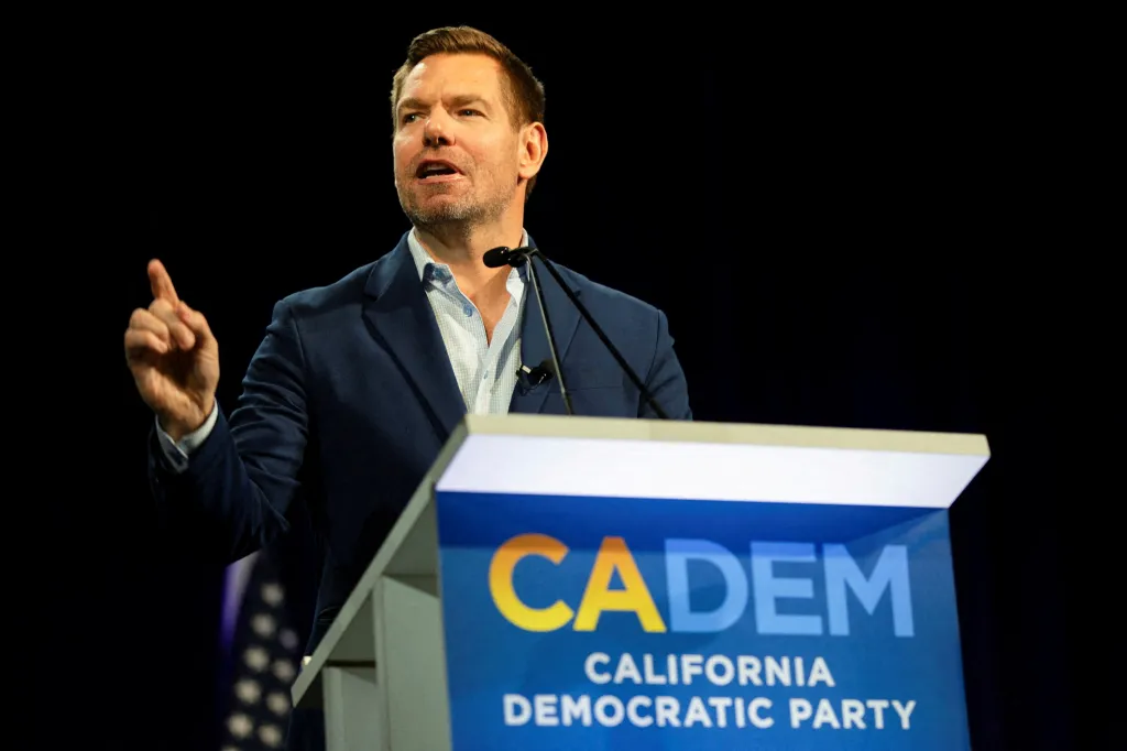 U.S. Representative Eric Swalwell speaking at a podium with a blue sign that says
