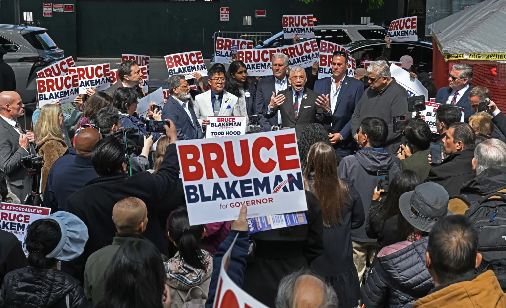 Bruce Blakeman speaking at a protest against a homeless shelter, with attendees holding signs for 