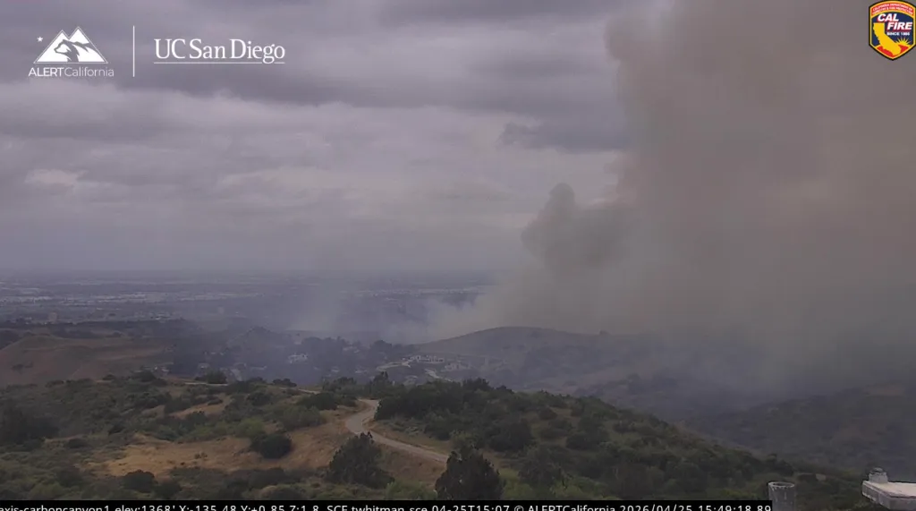 Alert California view of the Carbon Canyon fire showing heavy smoke rising from hills with scattered buildings.