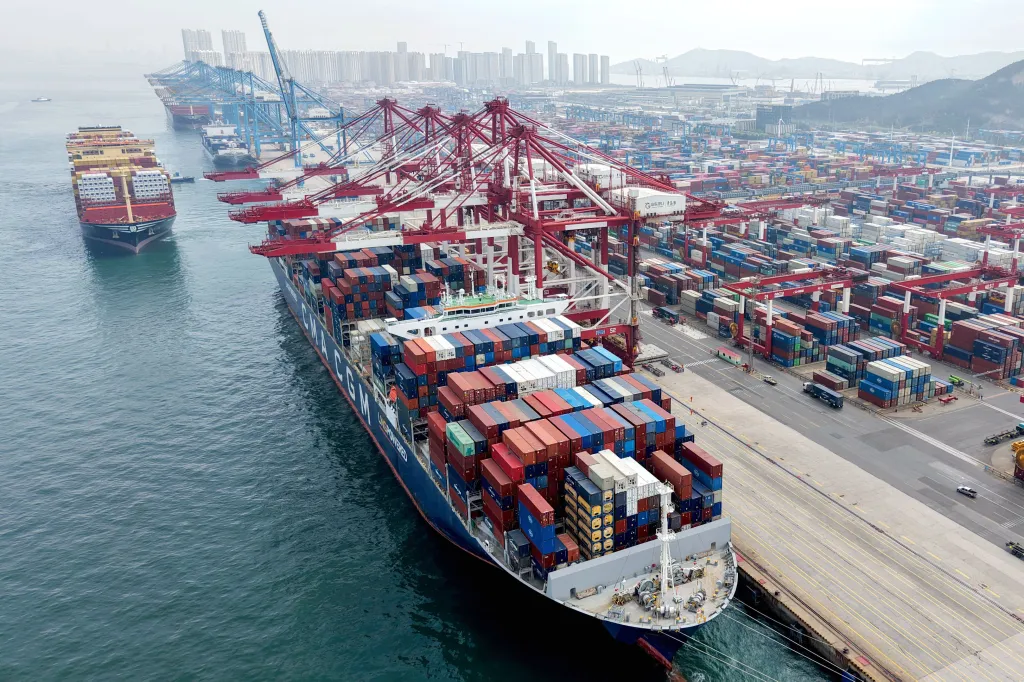 Cargo ships docked at a port in Qingdao, China, with cranes overhead and shipping containers covering the dock.