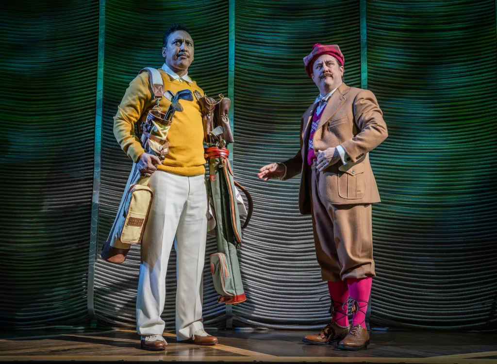 Two actors from 'Fallen Angels' on Broadway are dressed in vintage golf attire and stand on a stage.