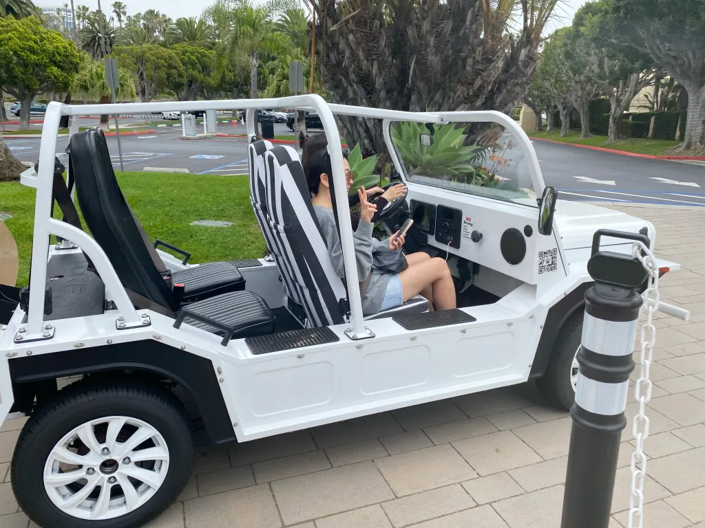A woman sitting in a white electric Moke vehicle that resembles a golf cart.